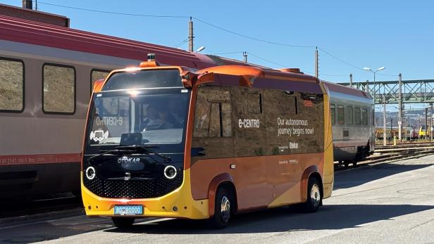 Neuer gelb-orangener ÖBB E-Postbus vor Zug
