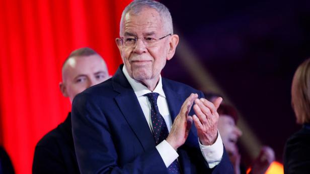 Alexander Van der Bellen klatscht vor einem roten Hintergrund in die Hände.