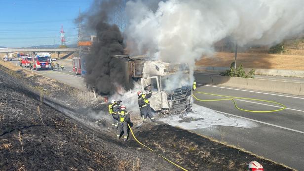 Feuerwehrleute löschen einen ausgebrannten Lkw auf der S1, während dichter Rauch von der Böschung aufsteigt.