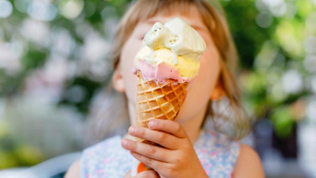 Little preschool girl eating ice cream in waffle cone on sunny summer day. Happy toddler child eat icecream dessert. Sweet food on hot warm summertime days. Bright light, colorful ice-cream