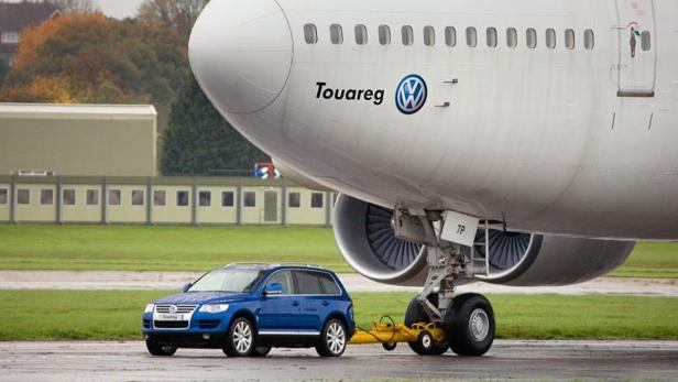 Ein blauer VW Touareg zieht ein riesiges Passagierflugzeug auf der Startbahn.