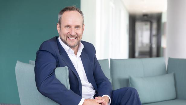 Lächelnder Mann im blauen Anzug sitzt auf einem hellgrünen Sofa in einem modernen Büro.