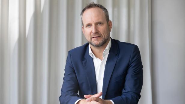 Mann im blauen Anzug sitzt am Tisch und blickt ernst in die Kamera.
