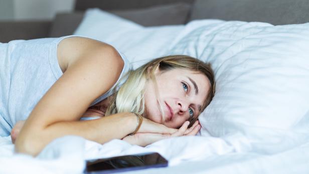 Mid adult woman lying in bed with mobile in depression