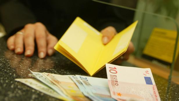 Eine Person hantiert mit einem gelben Impfpass und Euro-Banknoten.