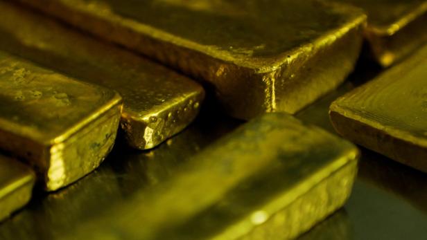 Mehrere glänzende Goldbarren liegen gestapelt auf einer metallischen Oberfläche.