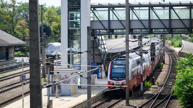 Ein rot-weißer ÖBB-Zug fährt in den Bahnhof Liesing ein, über dem eine gläserne Fußgängerbrücke verläuft.