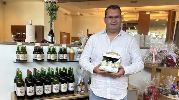 Saftproduzent Martin Trummer weißem Hemd hält eine Geschenkbox mit Flaschen in einem Laden für Getränke und Geschenkkörbe.