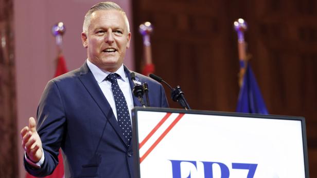 Mann im Anzug spricht an einem Rednerpult vor Mikrofonen und FPÖ-Logo.