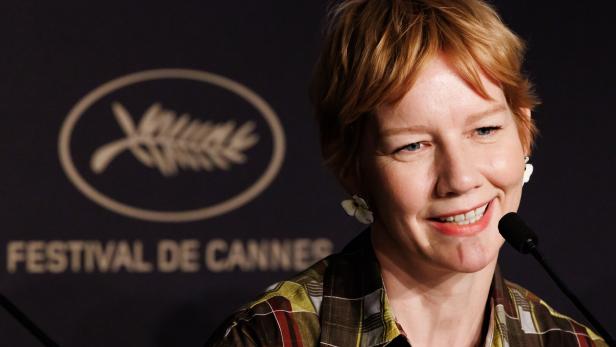 Sandra Hüller lächelt vor dem Logo des Festival de Cannes in ein Mikrofon.