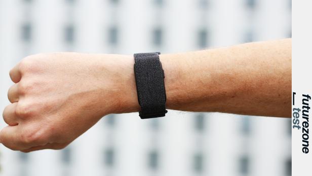 Ein Arm mit schwarzem Fitnessarmband vor unscharfem Hintergrund.