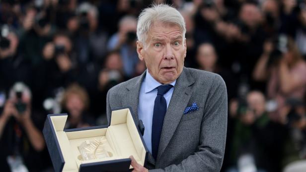 Harrison Ford hält mit überraschtem Gesichtsausdruck die Goldene Palme bei den Filmfestspielen von Cannes in die Kamera.