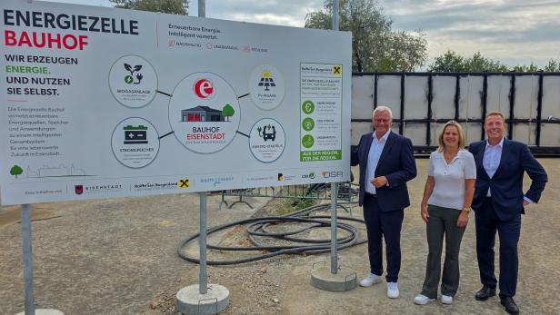 Drei Personen stehen vor einem Schild zur Energiezelle Bauhof Eisenstadt mit Grafiken zu Biogas, PV-Anlage und Speicher.