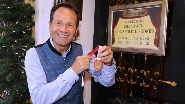 Alexander Rüdiger hält eine Medaille vor einem Bilderrahmen mit Schrift