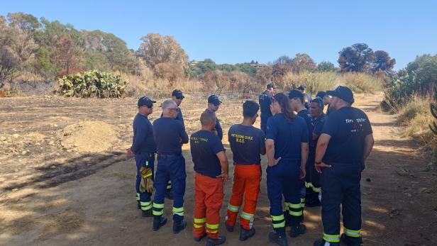 Mehrere Feuerwehrleute stehen in einer kargen Landschaft im Kreis.