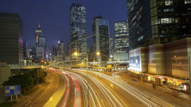 Nachts beleuchtete Skyline von Hongkong mit viel befahrenen Straßen.