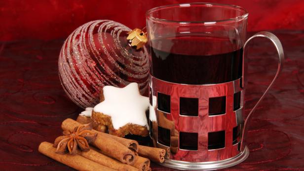 Ein Glas Glühwein mit Zimtstangen, Sternanis, Zimtsternen und einer roten Weihnachtskugel.