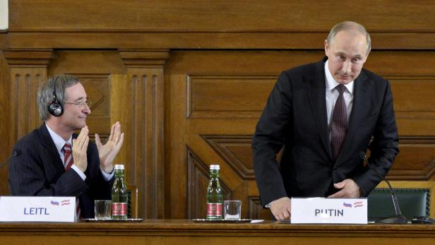 Wladimir Putin und ein weiterer Mann sitzen an einem Tisch bei einer Konferenz.