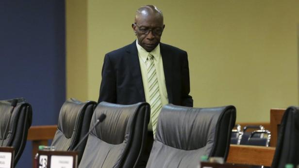 Ein Mann mit Brille und Anzug steht in einem Konferenzraum vor leeren Stühlen.