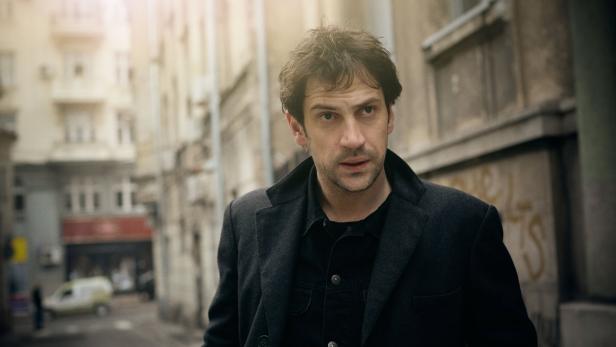 Ein Mann mit dunkler Jacke steht in einer Gasse.