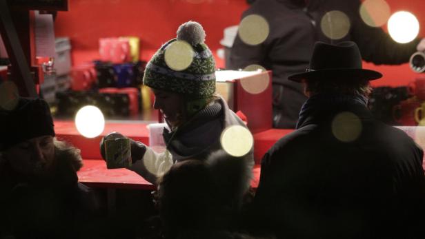 Eine Frau mit Mütze trinkt auf einem Weihnachtsmarkt etwas Warmes.