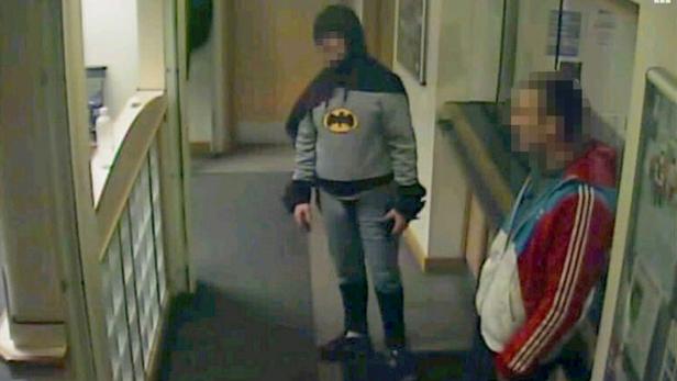 A man dressed as Batman and a burglary suspect stand in a police station in Bradford, northern England, on February 25, 2013, in this still photograph taken from video and provided by West Yorkshire Police on March 4, 2013. A mystery man dressed as Batman demonstrated the same crime-fighting skills as the caped crusader when he handed over a suspect wanted for burglary in Britain. Closed-circuit television footage showed a portly figure wearing an ill-fitting costume including gloves, cape and mask, bringing a 27-year-old man to a police station in Bradford in northern England. REUTERS/West Yorkshire Police/Handout (BRITAIN - Tags: CRIME LAW SOCIETY) PICTURE PIXELATED AT SOURCE. ATTENTION EDITORS - THIS IMAGE WAS PROVIDED BY A THIRD PARTY. FOR EDITORIAL USE ONLY. NOT FOR SALE FOR MARKETING OR ADVERTISING CAMPAIGNS. THIS PICTURE IS DISTRIBUTED EXACTLY AS RECEIVED BY REUTERS, AS A SERVICE TO CLIENTS
