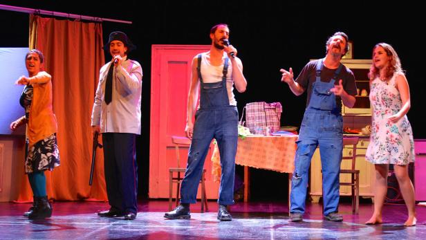 Fünf Darsteller stehen auf einer Bühne und singen in Mikrofone.