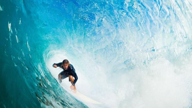 Ein Surfer reitet auf einer Welle in einem türkisblauen Ozean.