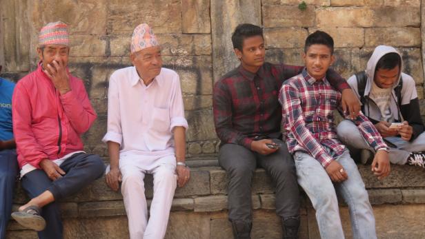 Eine Gruppe von Männern sitzt an einer Steinmauer.