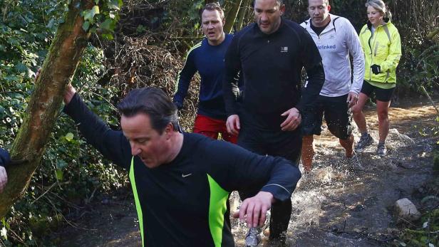 David Cameron und andere Personen durchwaten einen Bach.