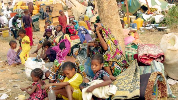 Eine Gruppe von Frauen und Kindern sitzt im Freien inmitten von Habseligkeiten.