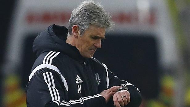 Ein Mann in einer Adidas-Jacke blickt auf seine Armbanduhr.