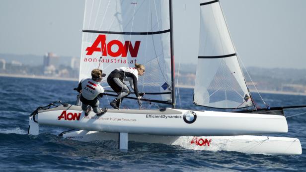 Zwei Segler auf einem Katamaran mit dem AON-Logo segeln auf dem Meer.
