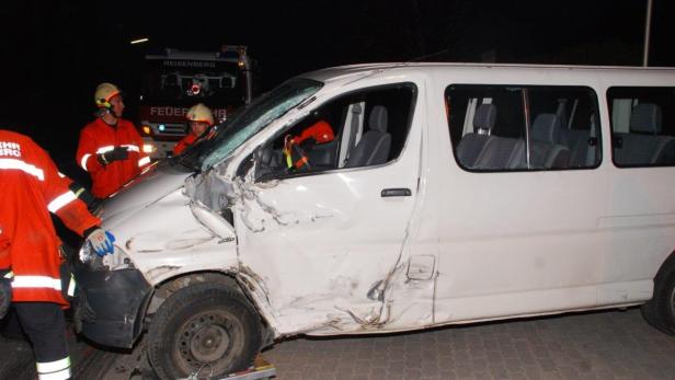 Ein weißer Transporter mit schweren Unfallschäden und Feuerwehrleuten vor Ort.
