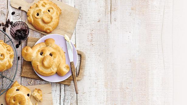 Mehrere süße Schweinebrötchen mit Rosinenaugen liegen auf einem Tisch.