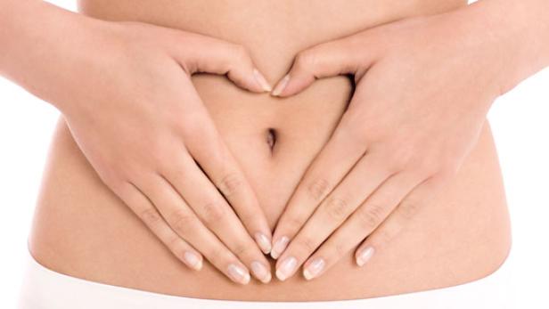 Eine Frau formt mit ihren Händen ein Herz über ihrem Bauch.