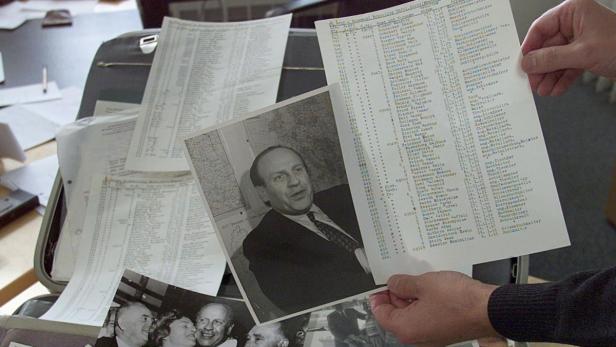 Eine Person hält ein Foto eines Mannes und eine Liste mit Namen in der Hand.