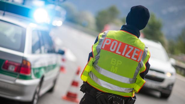 Ein Polizist steht an einer Straßensperre mit einem Polizeiauto im Hintergrund.
