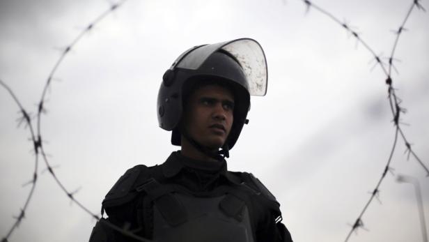 Ein Mann in Schutzkleidung steht vor einem Stacheldrahtzaun.