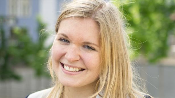 Eine lächelnde junge Frau mit blonden Haaren blickt in die Kamera.