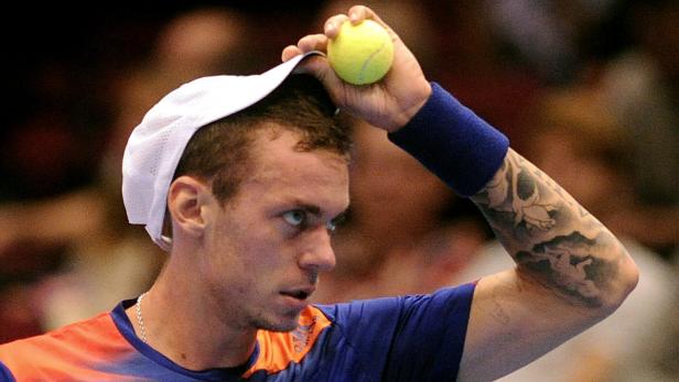 Ein Tennisspieler mit Tätowierung balanciert einen Tennisball auf seiner Mütze.