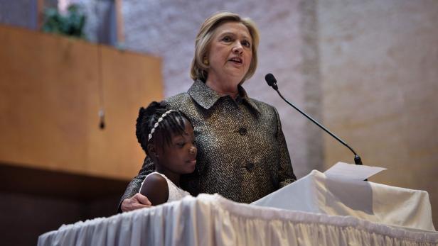 Hillary Clinton hält eine Rede mit einem jungen Mädchen am Rednerpult.