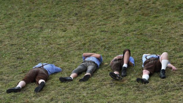 Vier Männer in Lederhosen liegen auf einer Wiese.