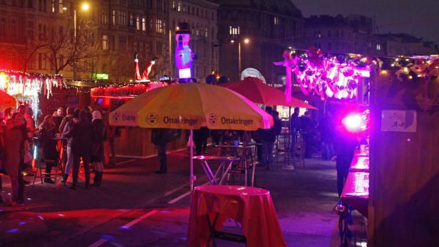 Ein belebter Weihnachtsmarkt mit Menschen, Ständen und festlicher Beleuchtung in der Nacht.