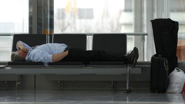 Ein Mann schläft auf einer Bank in einem Wartebereich, neben ihm sein Gepäck.
