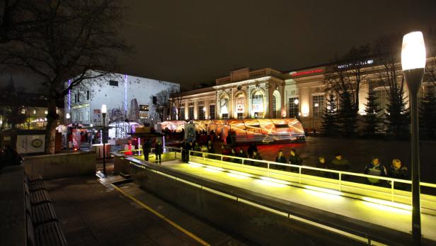 Die Kunsthalle Wien ist nachts beleuchtet, mit Menschen auf einer Rampe im Vordergrund.