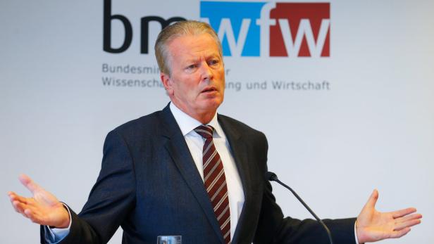 Ein Mann in Anzug gestikuliert vor dem Logo des BMWFW.