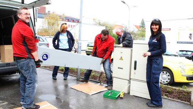 Mitarbeiter installieren ein neues Schild an einem Stromverteilerkasten der BEWAG.