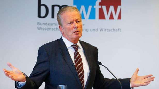Ein Mann in Anzug gestikuliert vor dem Logo des BMWFW.