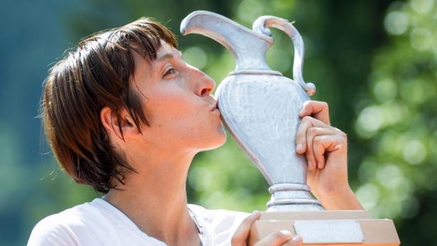 Eine Frau küsst eine silberne Trophäe vor einem grünen Hintergrund.